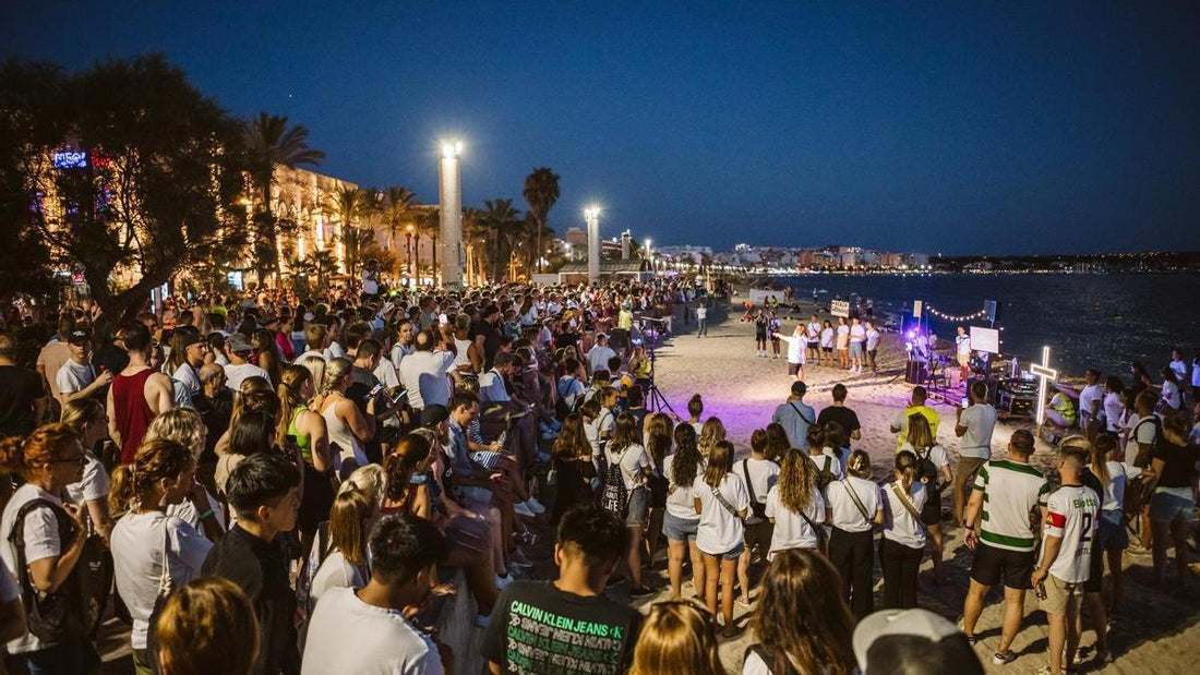 Große Menschenmenge versammelt sich am Strand von El Arenal, Mallorca, bei Nacht für eine Veranstaltung, beleuchtet von Straßenlaternen und Lichtern entlang der Promenade.